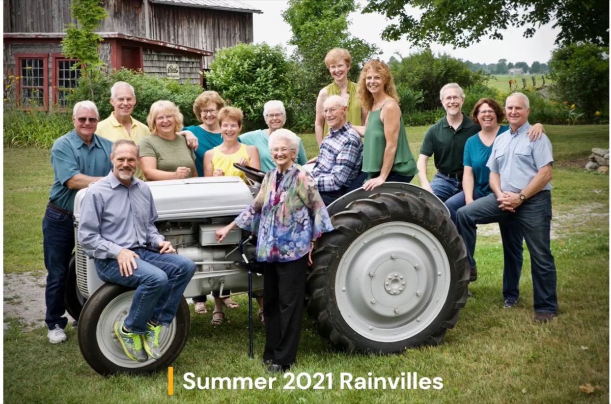 The Rainville family, summer 2021 — fifteen family members gathered around a vintage tractor in front of the barn on the family farm.